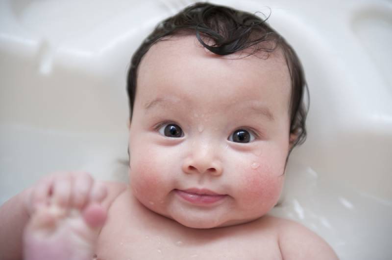 baby smiling and grabbing his toes in a tub