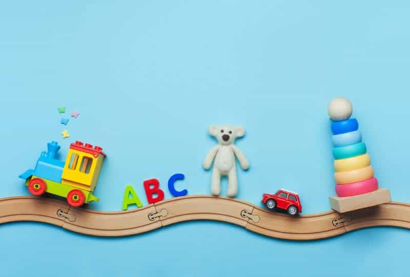 Kids toys train, ABC letters, bear, car and pyramid on toy wooden railway on blue background 