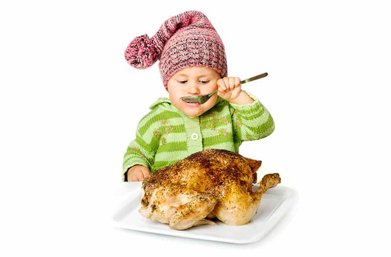 isolated baby with big baked chicken pretending to eat with spoon