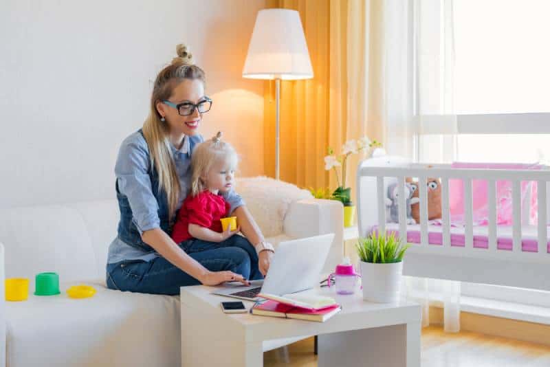 Stay at home mom working on laptop with kid on her lap in her living room