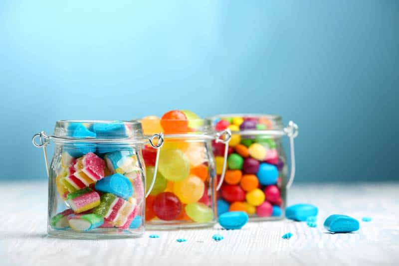 Colorful candies in jars on table on blue background 
