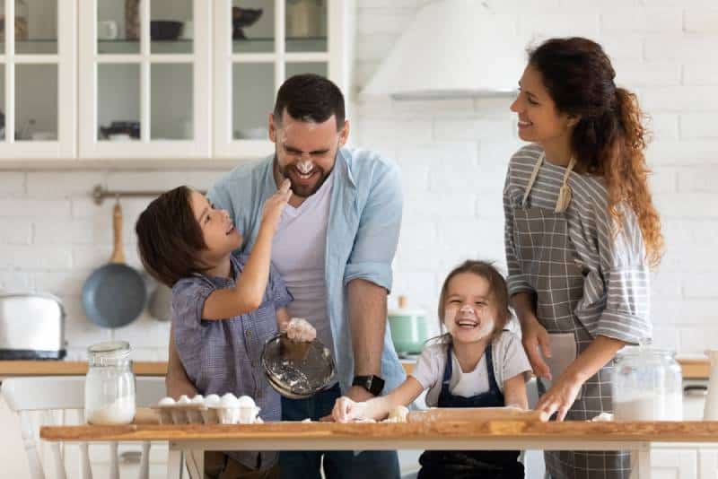 Happy smiling parents enjoy weekend play with small children doing bakery cooking in kitchen