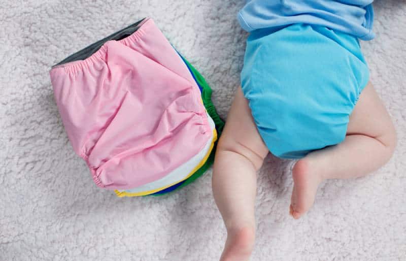 folded cloth diapers next to a baby in bed