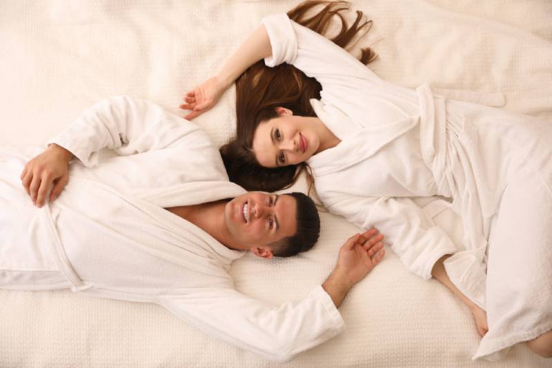 Happy couple in white bathrobes lying on bed