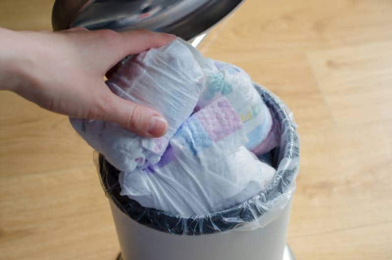 Woman hand put used diaper to the Trash bin full of used diapers