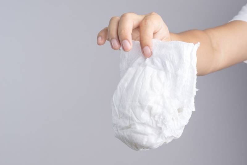 Hand holding used white baby diaper on grey background