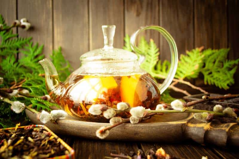 Herbal tea in a glass teapot with herbs and lemon on dark rustic background