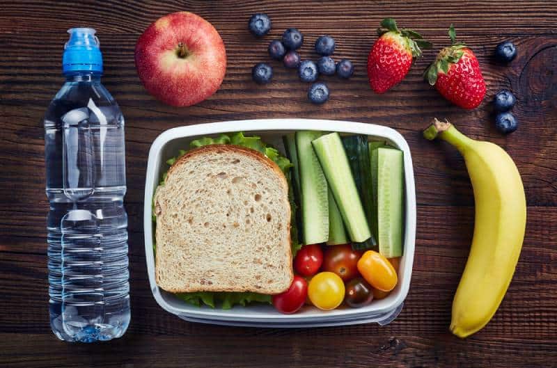 Healthy lunch box with sandwich and fresh vegetables, bottle of water and fruits on wooden background