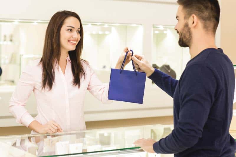 female jeweler passing a bag with purchases to her male customer man buying jewelry