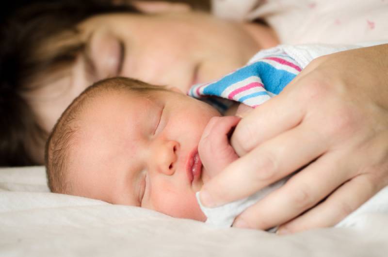 Newborn infant child resting next to mother on bed
