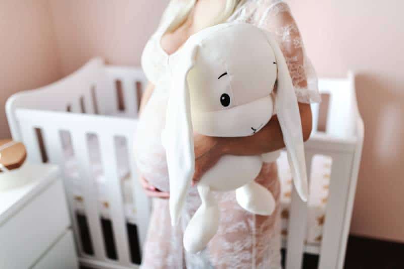 Close up of pregnant woman holding white bunny toy while standing in baby room