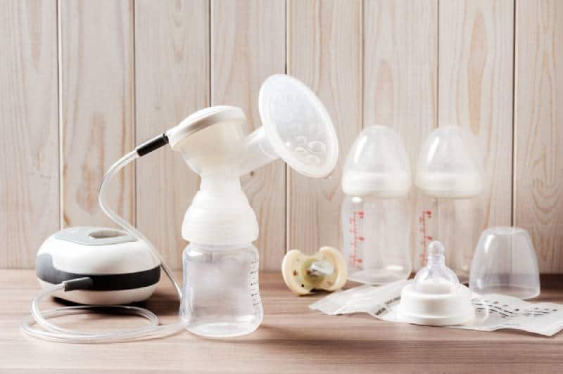 Breast pump and baby bottles on wood background