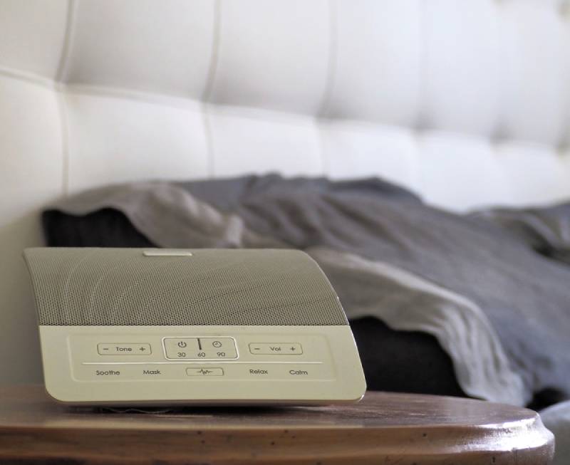 White noise machine on a table next to a bed