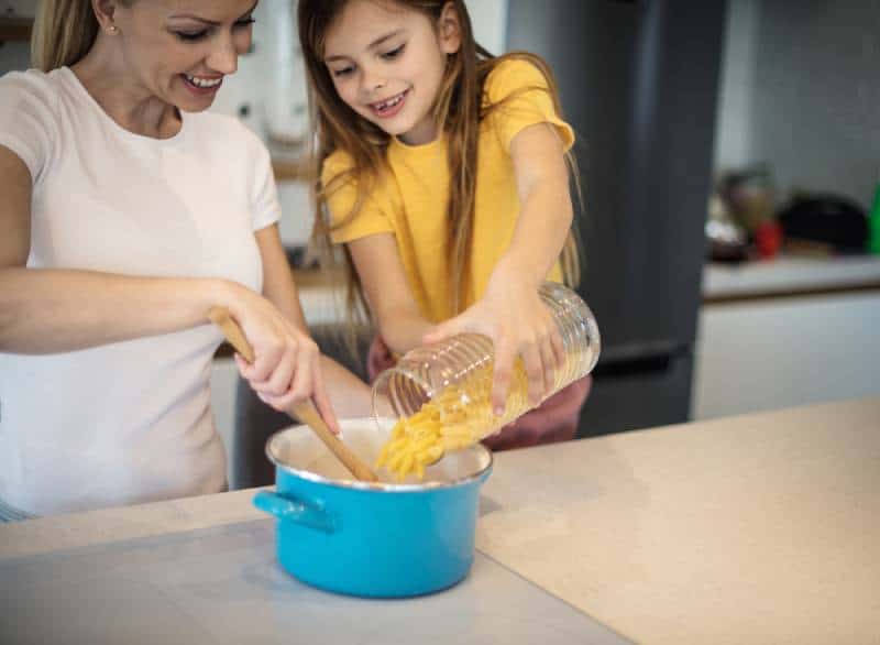 Happy mother and daughter preparing pasta in their kitchen