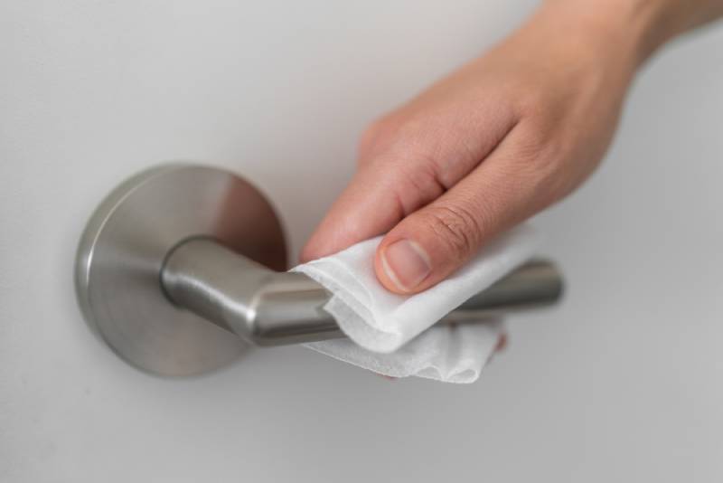 woman wiping doorknob with antibacterial disinfecting wipe for killing bacteria