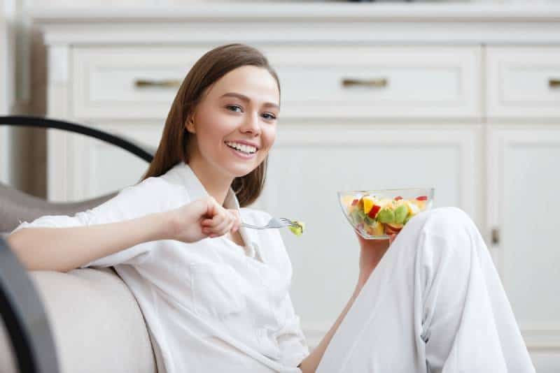 Young woman in white eating healthy fruit breakfast in bowl at home