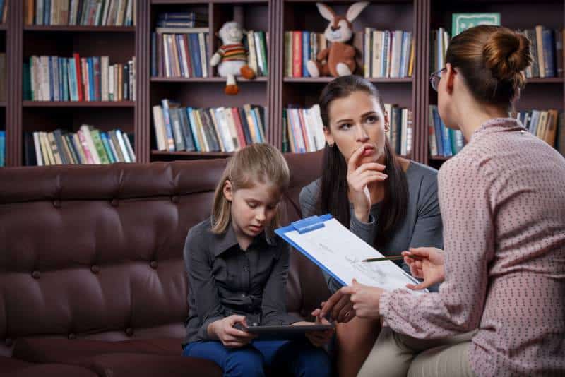Young mom with her daughter talking to a teacher in her office