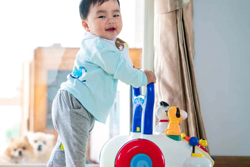 cute asian baby standing by activity table on wheels