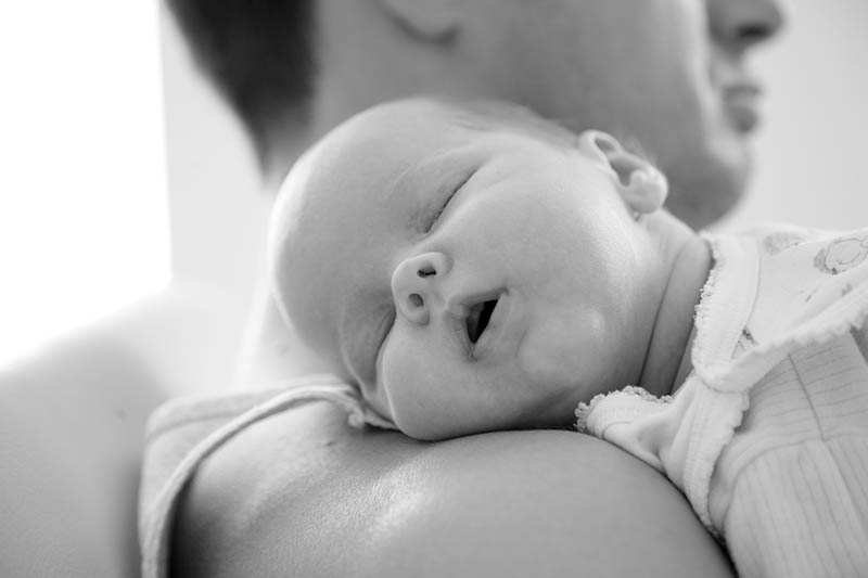 black and white photo of baby sleeping with open mouth on dad's shoulder