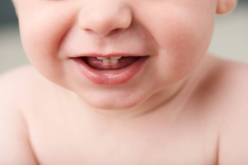 image of a baby's mouth open showing his first teeth, nose and his upper body