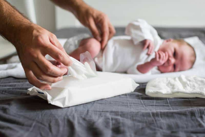 Father changing newborn baby's diaper and taking a wet wipe to clean the baby on bed