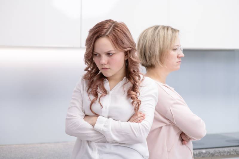 girl stands with her back to her mother with a displeased expression on her face at home