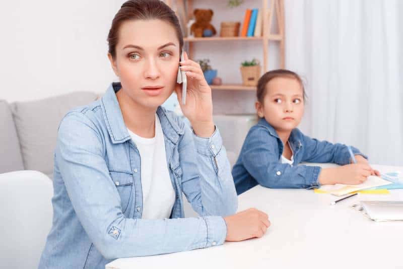mom sitting at table with her daughter and talking on phone 