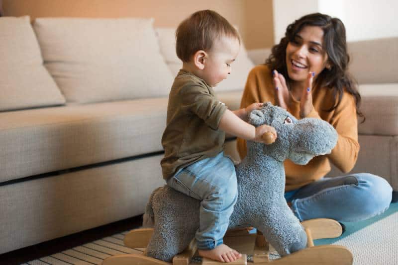 Baby boy playing with a rocking horse with mom's help indoors