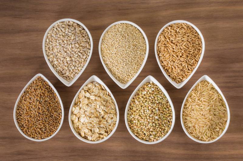 An assortment of whole grains in bowls over a wooden background