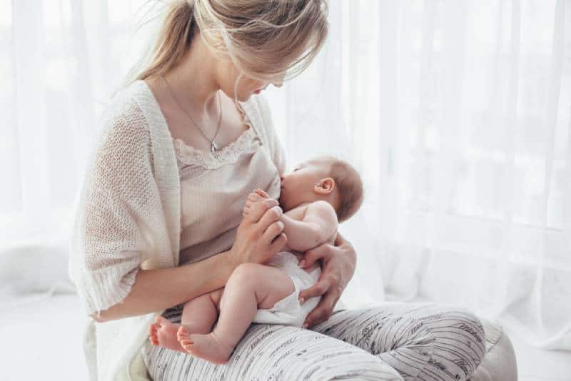 mom breast feeding baby while sitting on a bed indoors