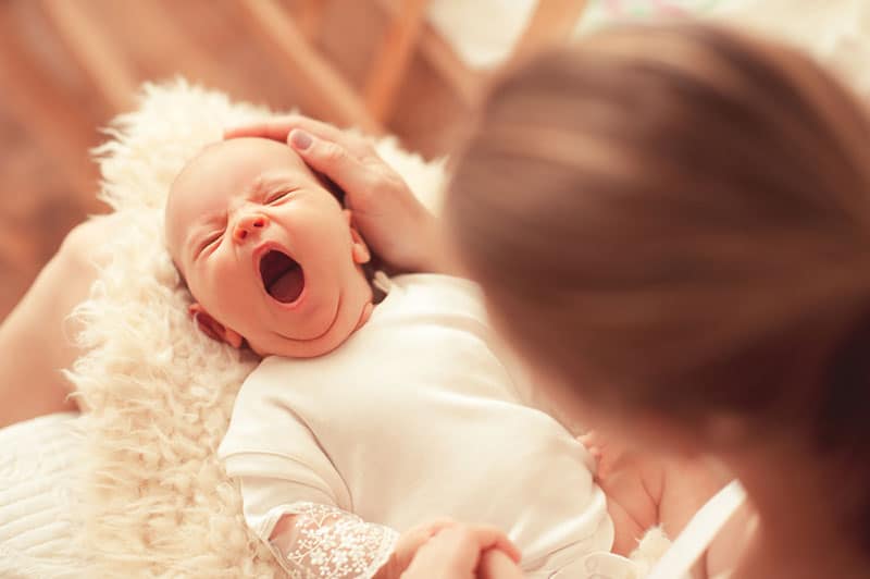 mother holding yawning baby