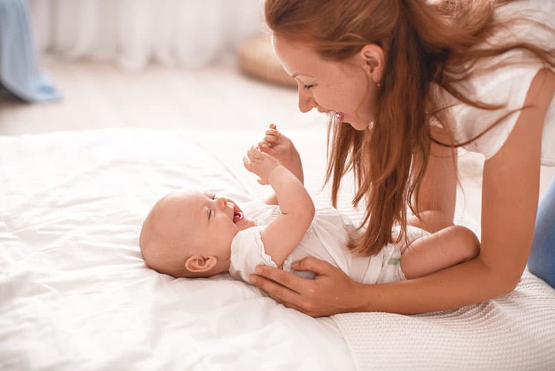 mother playing with baby on the bed