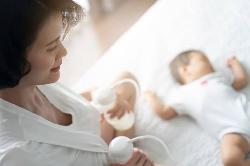 mother pumping breast milk with baby next to her