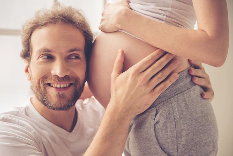 smiling man hugging pregnant woman belly