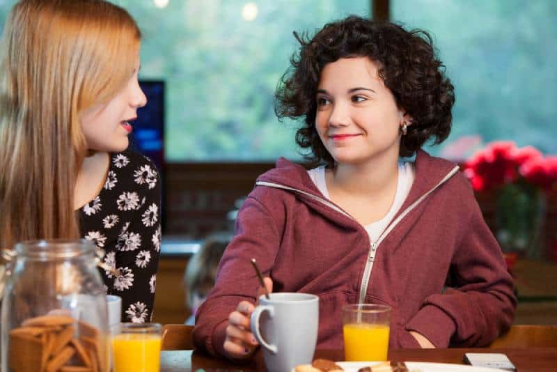Two happy teen girl friends having breakfast together at home