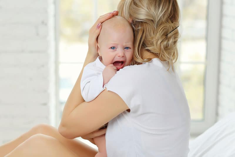 young blond woman holding crying baby in bed