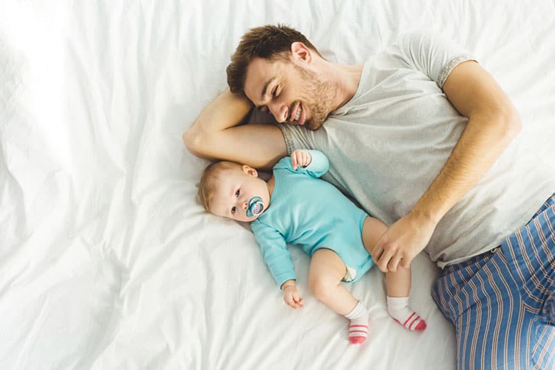 young father lying with his baby on bed