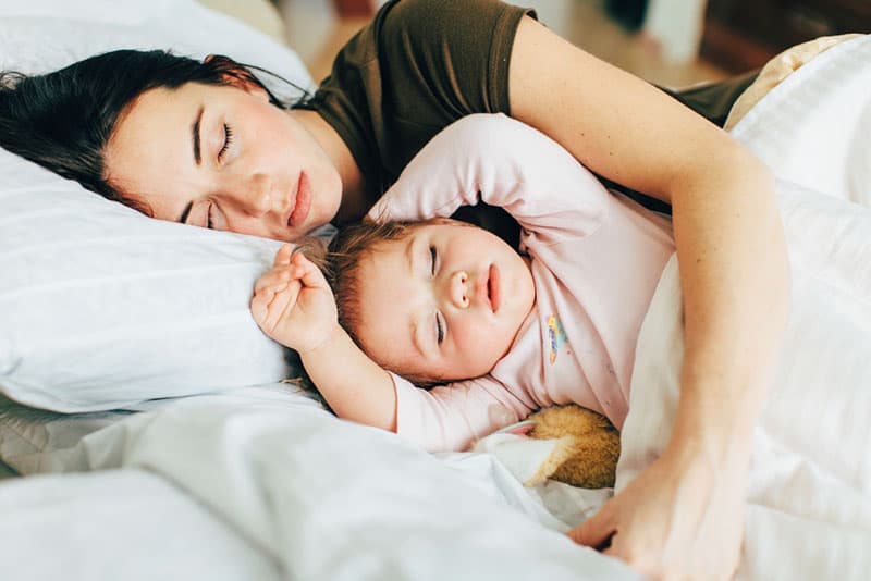 young mother and baby sleeping together in bed