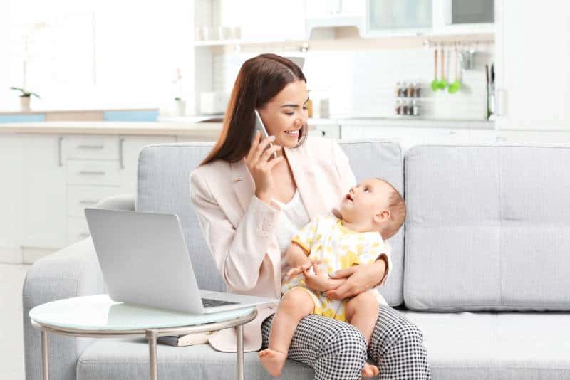 Mom holding baby and talking on phone at home