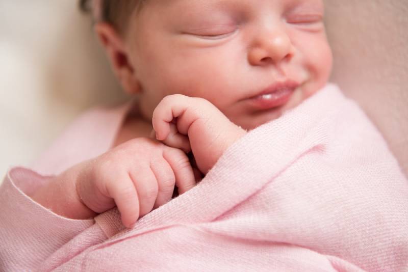Newborn baby girl asleep on a pink blanket.