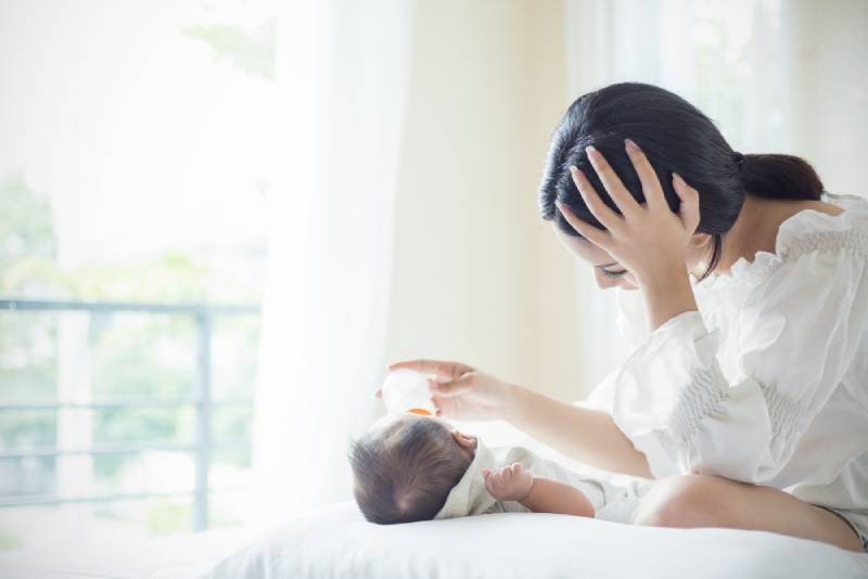 Woman is bottle-feeding her baby while sitting on bed