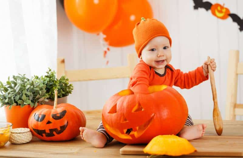 happy baby in costume with a pumpkin for Halloween