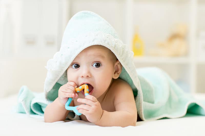baby lying on bed with teether in mouth