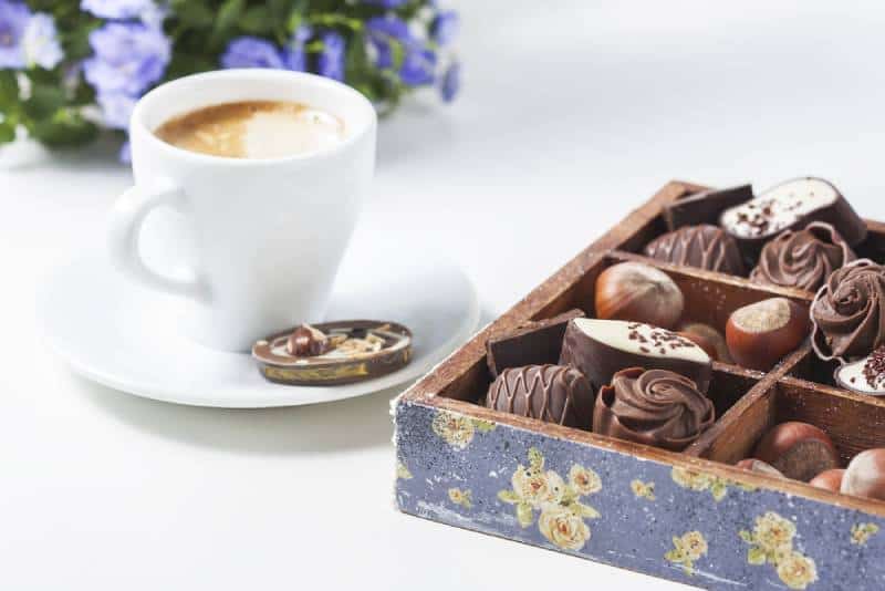 Cup of coffee on a white background with a variety of chocolates in a wooden box