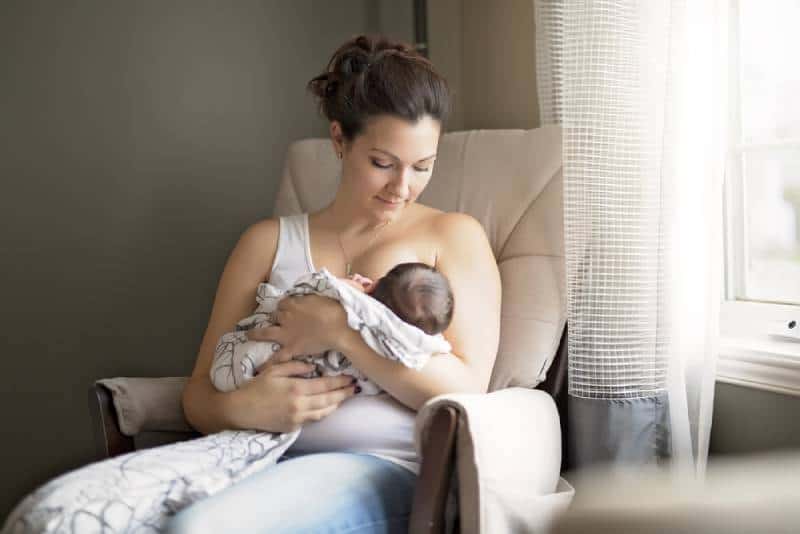 Mother breastfeeding her little baby boy in her arms while sitting in a chair