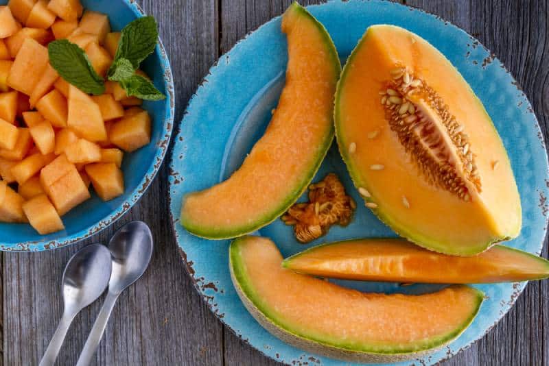 Cantaloupe melon slices sitting on blue rustic plate on wooden tabletop 