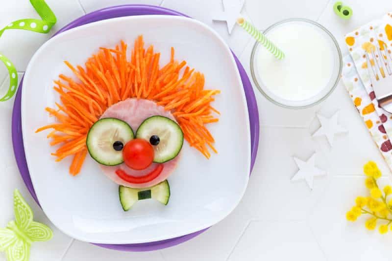 cute smiling clown face on ham sandwich decorated with fresh cucumber, carrots and tomatoes 