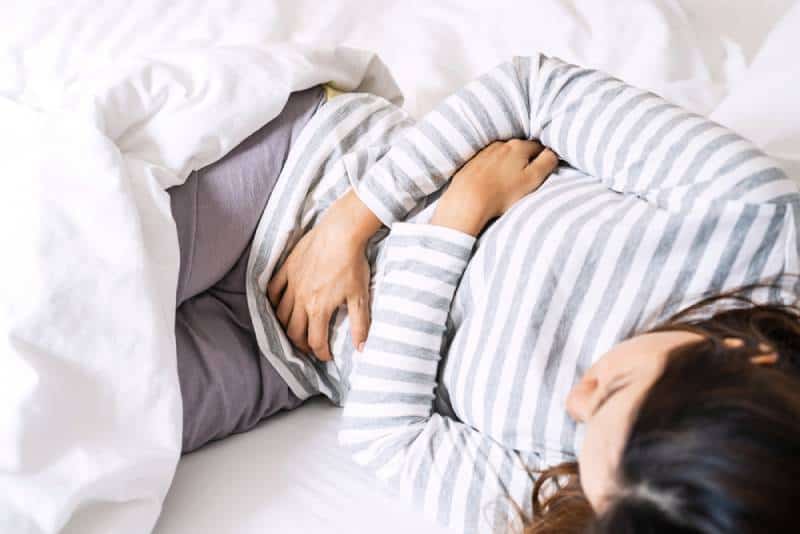 Girl holding her belly and lying in bed at home
