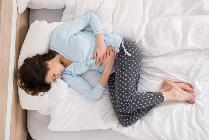 Girl with stomach pain lying in bed at home