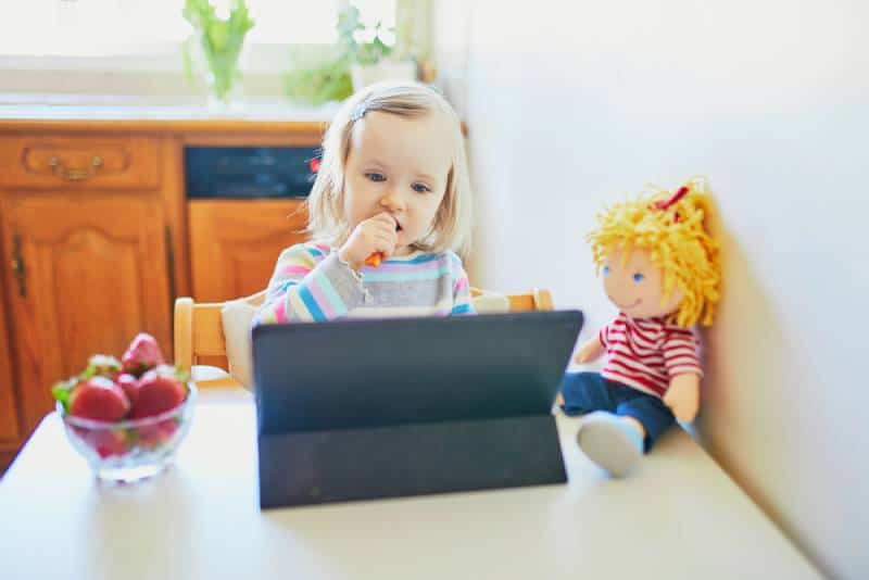  toddler girl eating fresh strawberries and using tablet at home